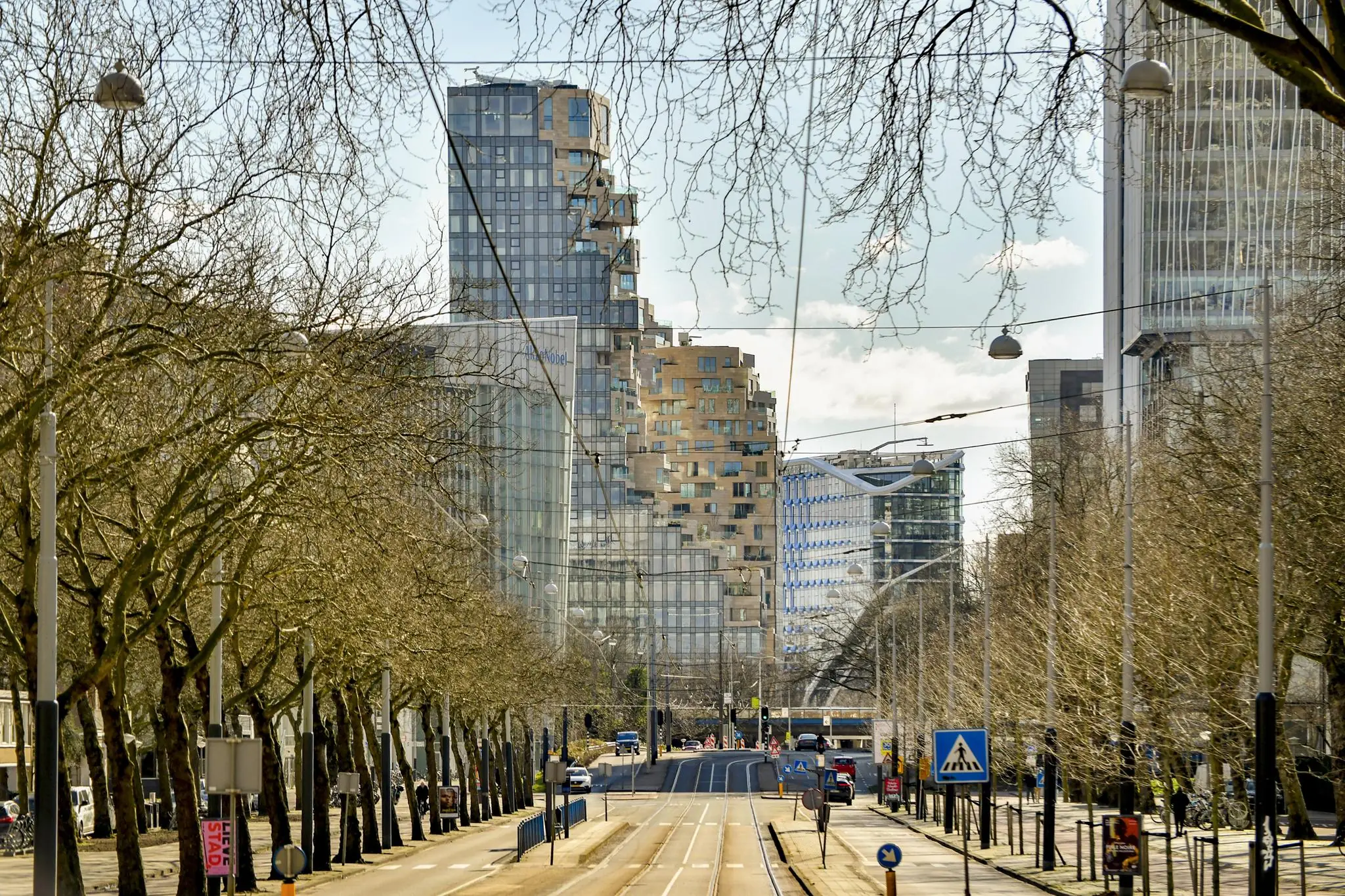 Uitzicht op de Cornelis Dopperkade in Amsterdam met moderne hoogbouw en kale bomen langs de trambaan.